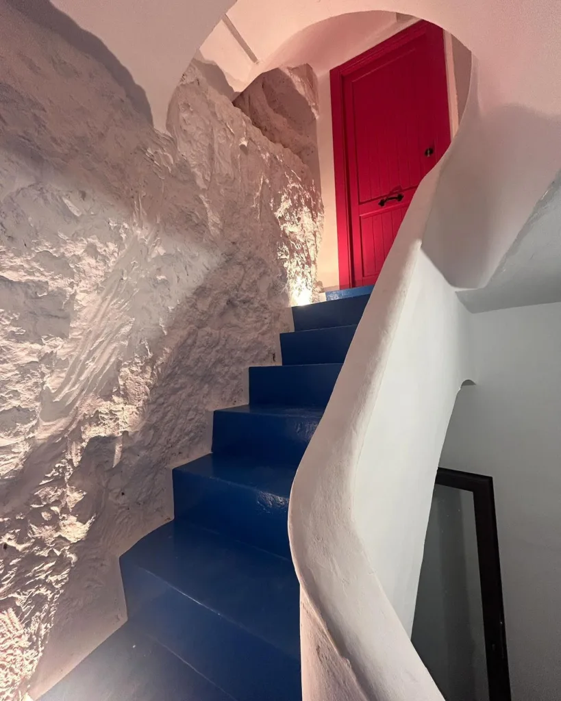Puerta de una de las casas de Alcalá al cielo pintada de rojo, las escaleras son azules y las paredes son de roca blanca ya que están dentro de una montaña.