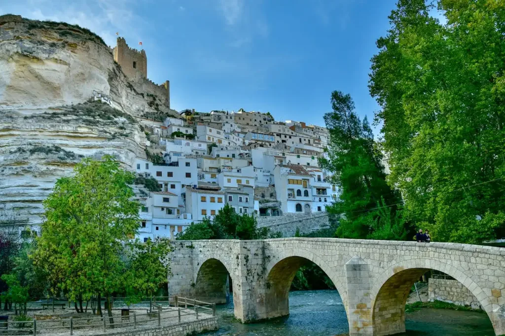 Imagen de Alcalá del Júcar en la que se puede ver el puente y las casas blancas de fondo. También se puede observar el castillo de Alcalá.