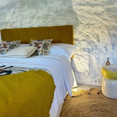 Imagen de la cama de Frida con detalles amarillos y una luz en el suelo que le da un ambiente natural a la habitación. Las paredes son de roca blanca ya que esta dentro de una montaña.