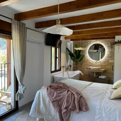 Imagen de la casa Coquette, en la que se ve la amplica cama, la bañera hidromasaje al lado de la cama y el lavamanos al lado, con un espejo con luz redondo encima del lavamanos, también se puede apreciar la televisión y el aire acondicionado.