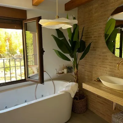 Ventana encima de la bañera hidromasaje con unas vistas espectaculares a la naturaleza. Hay una planta al lado de la bañera que le da una sensación de paz especial.